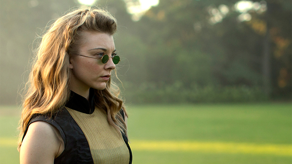 Natalie Dormer as Mrs Appleyard, with her hair loose, small sunglasses perched on her nose, wearing an anachronistic sleeveless dress with a mandarin collar and semi-transparent panel over her cleavage.